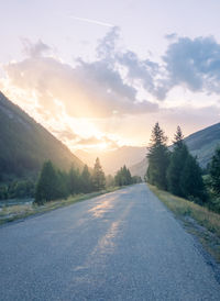 Road amidst trees against sky during sunset