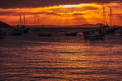 Sailboats moored on sea against dramatic sky during sunset