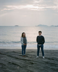 Full length of man and woman standing on beach against sky