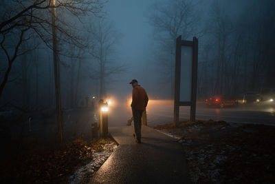 Rear view of man standing on street at night during winter