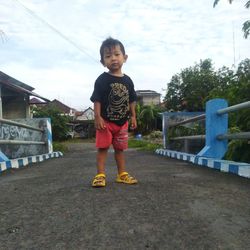 Full length of boy standing on riverbank against sky