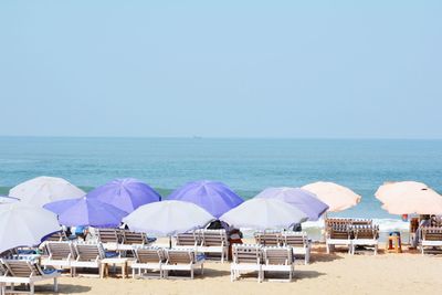 Parasols and lounge chairs at beach against clear blue sky