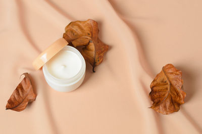 A jar of cream for dry skin care with dried autumn leaves on a wavy beige background