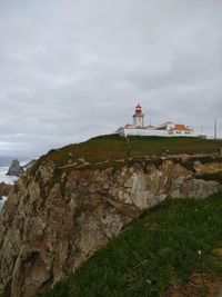 Lighthouse amidst rocks and buildings against sky