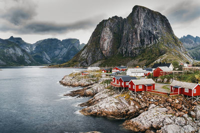 Houses on rock formation by river against cloudy sky