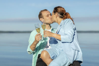 Happy international couple sitting on beach holding glasses of non-alcohol wine. caucasian man