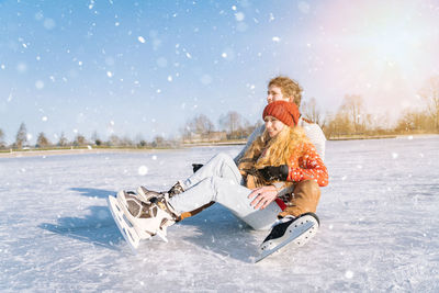 Full length of couple sitting on frozen lake during winter