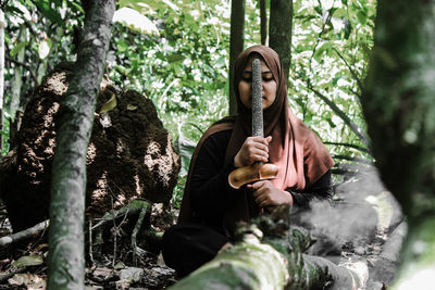 Portrait of woman sitting by tree trunk in forest