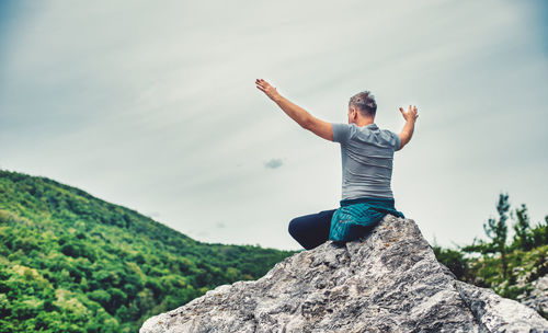 Full length of man with arms raised on rock against sky