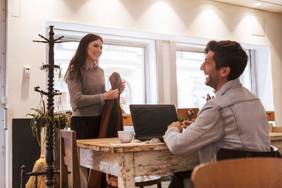 Happy man with laptop looking at female friend in cafe