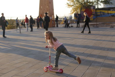 Full length of cute girl playing with push scooter on street