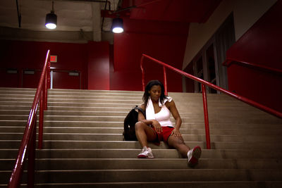 Woman looking leg while sitting on stairs in stadium