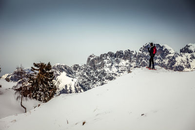 Person walking on snowcapped mountain against sky during winter