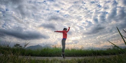 Side view of woman jumping on field against sky