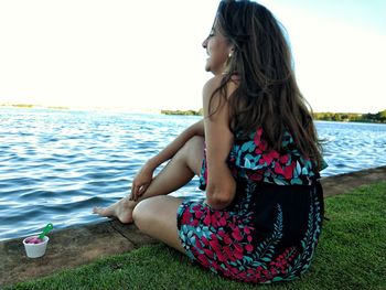 Woman sitting by sea against sky