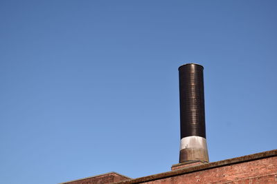 Low angle view of smoke stacks against clear blue sky