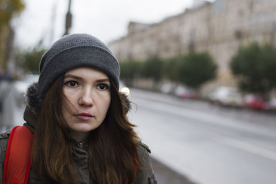 Beautiful young woman looking away on street against sky