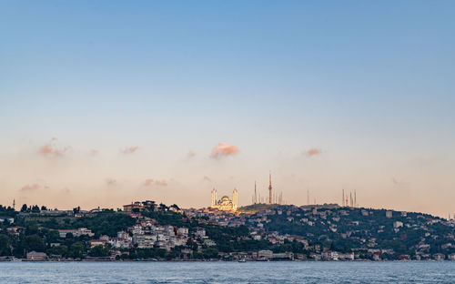 Sea by buildings against sky during sunset in city