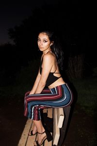 Side view portrait of young woman sitting on bench at night