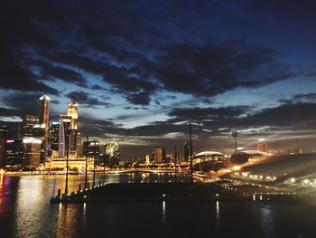 Illuminated buildings by river against sky at night