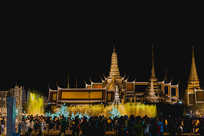 People at illuminated temple against building at night