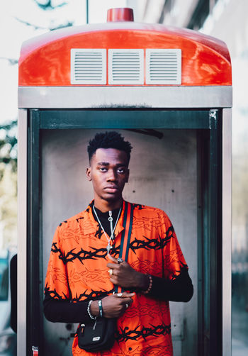 PORTRAIT OF A YOUNG MAN STANDING AGAINST ORANGE WALL