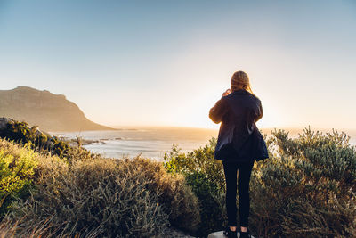 Rear view of woman standing by sea against sky