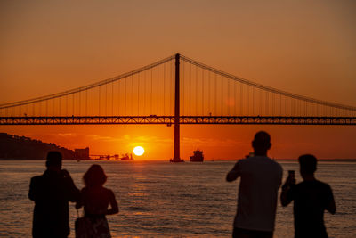 Silhouette people standing on suspension bridge at sunset