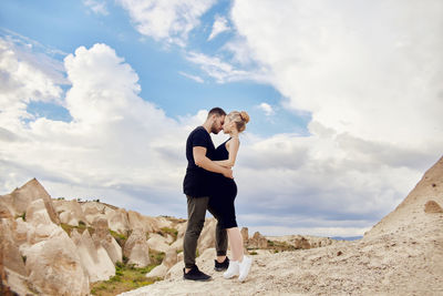Young couple standing on rock against sky