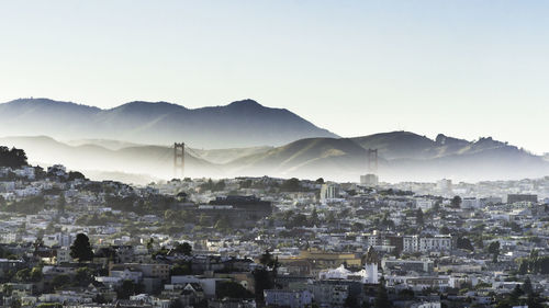 Cityscape by mountains against clear sky during foggy weather