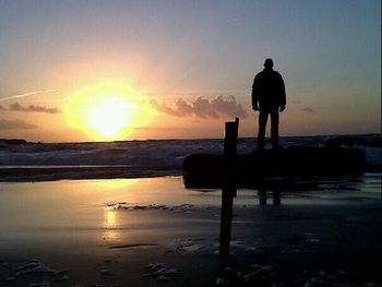 Silhouette people on beach in front of sea at sunset