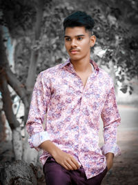 Handsome young man looking away while standing against tree