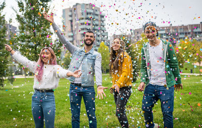 Cheerful friends throwing confetti while standing at park