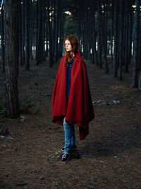 Portrait of woman standing by tree trunk in forest