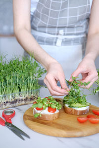 Woman preparing healthy sandwiches with microgreens and vegetables