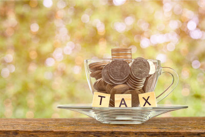 Close-up of coins with tax text in cup and saucer on table outdoors