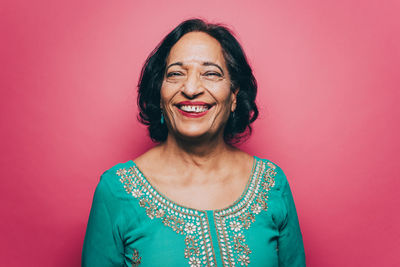 Portrait of smiling senior woman wearing salwar kameez against pink background