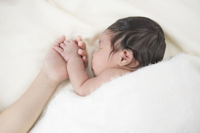 Cropped image of parent holding baby girl hand on bed