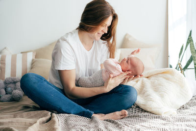 A tender caring mother nurses a newborn baby in her arms while sitting on the bed.