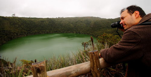 Side view of man photographing lake against sky