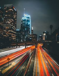 Light trails on road by illuminated buildings in city at night