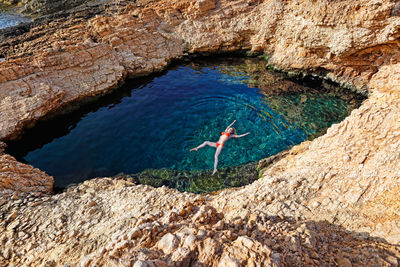 High angle view of woman floating on water amidst rock formation