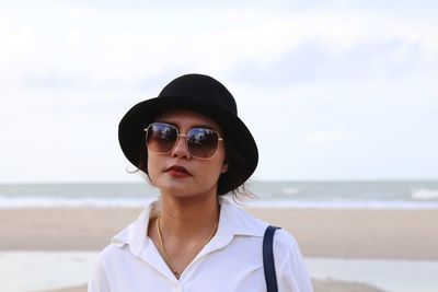 Portrait of woman wearing sunglasses while standing at beach against sky