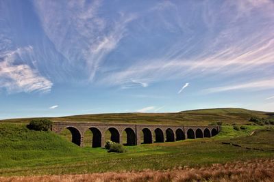 Arch bridge on field against sky