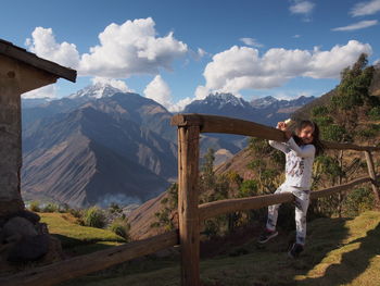 Portrait of cute girl sitting on wooden railing at mountains