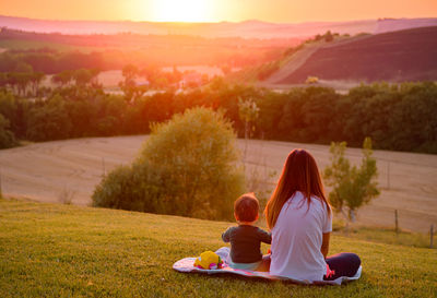 Rear view of women sitting on grass at sunset