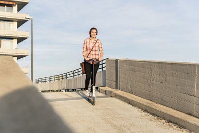 Young woman with headphones riding electric scooter on parking deck