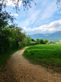 Dirt road amidst field against sky