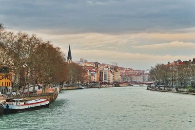 Boats in river by buildings in city against sky