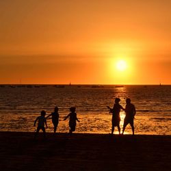 Silhouette of people at beach against orange sky